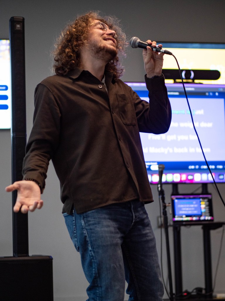Person singing with a microphone. TV screen with lyrics behind them to the right.