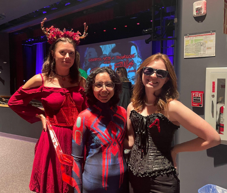 Three people in costumes, one wearing all red and a floral headband, one dressed as Spiderman, and the other wearing  a black corset and sunglasses.