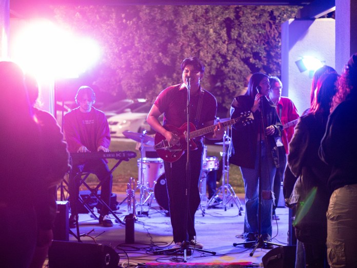 Band playing at an outside venue, backlit by pinkish lights.
