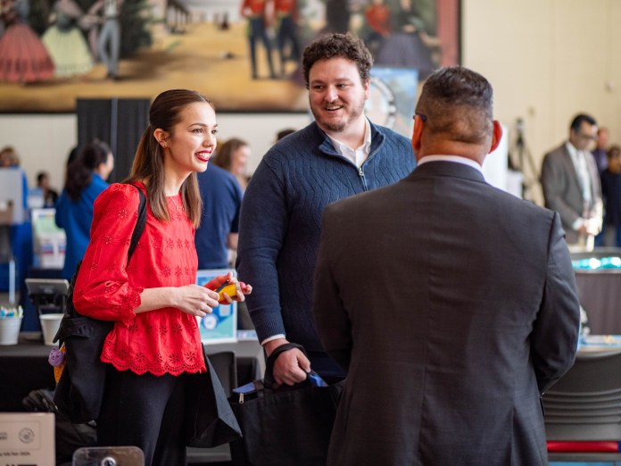 Two students talking to an employer at their table.