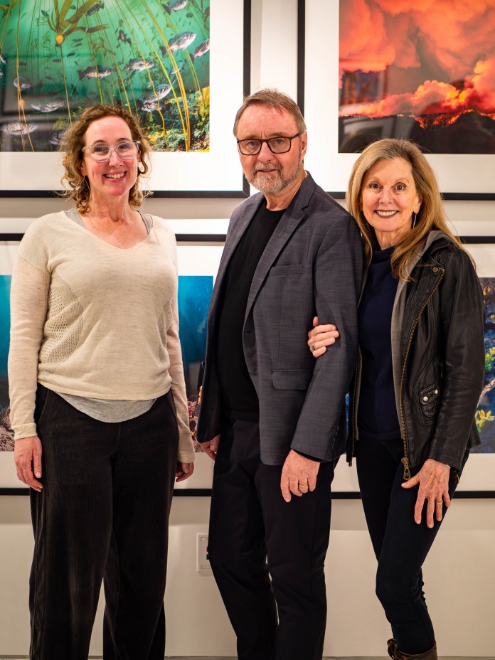 Three people posing in front of framed photography.