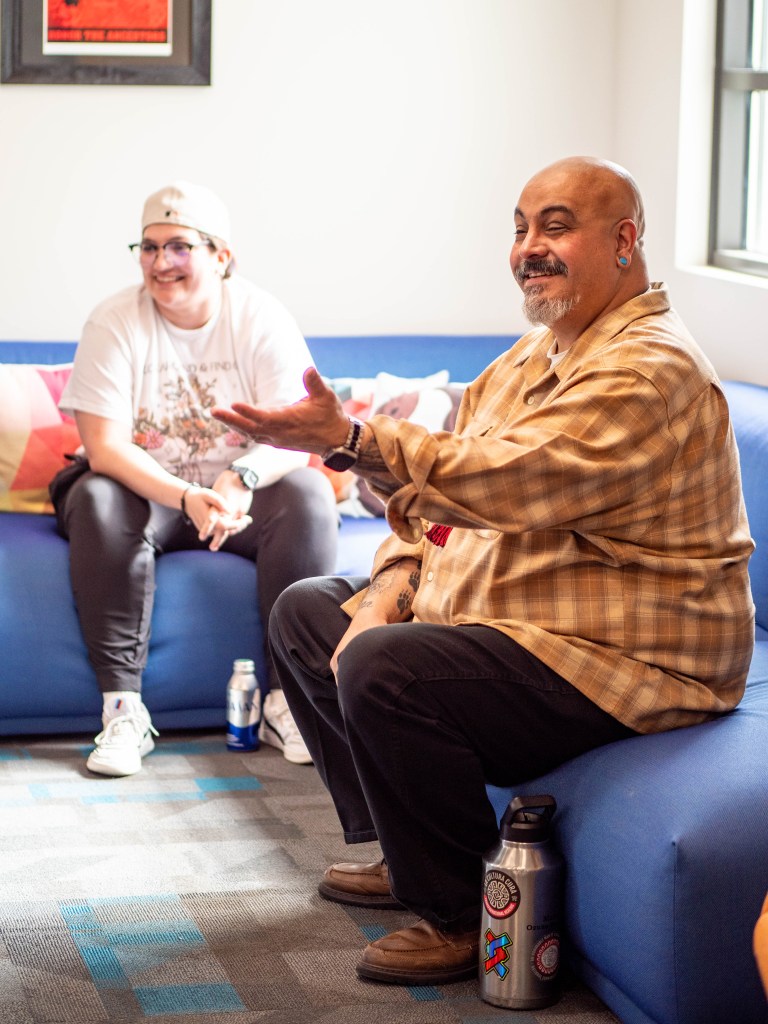 Ozuna-Sanchez sitting on a blue couch speaking with his arm outstretched.