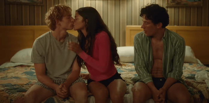 A teenage boy and girl kissing with another boy sitting next to them watching.