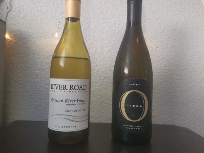 Green and yellow wine bottles, one with white label and dark text, the other with a black label and large gold 'O'. String lights in the background.