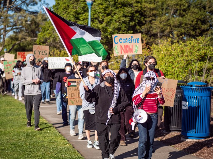 ADLC protesters marching holding signs and a Palestine flag.