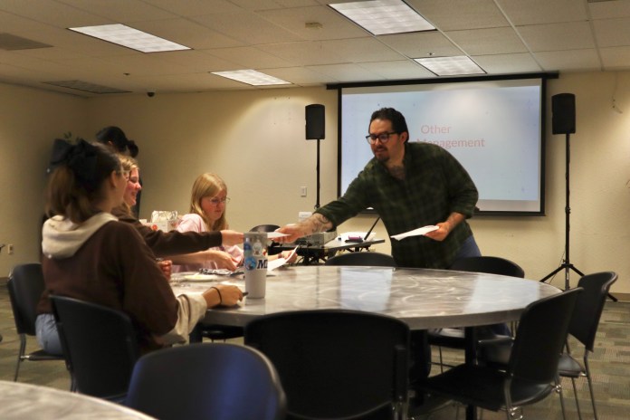 Photo of event staff handing out papers to a table group of students.