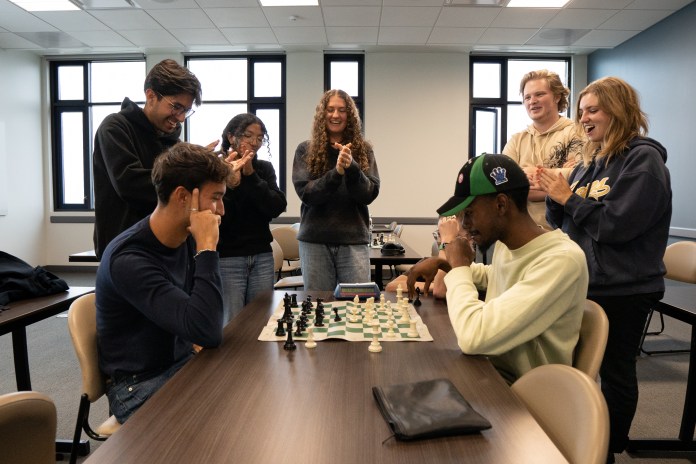 Photo of two people playing chess with 5 people watching the match