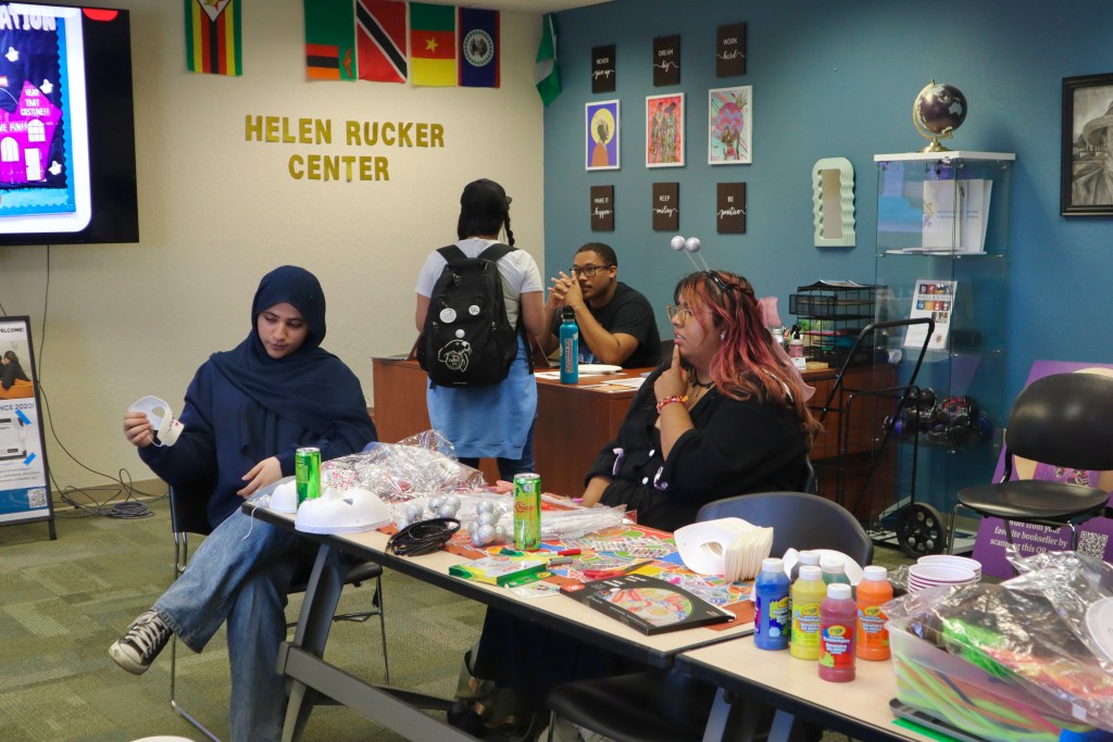 Picture of multiple students working on their masks as well as a student talking to staff at the event